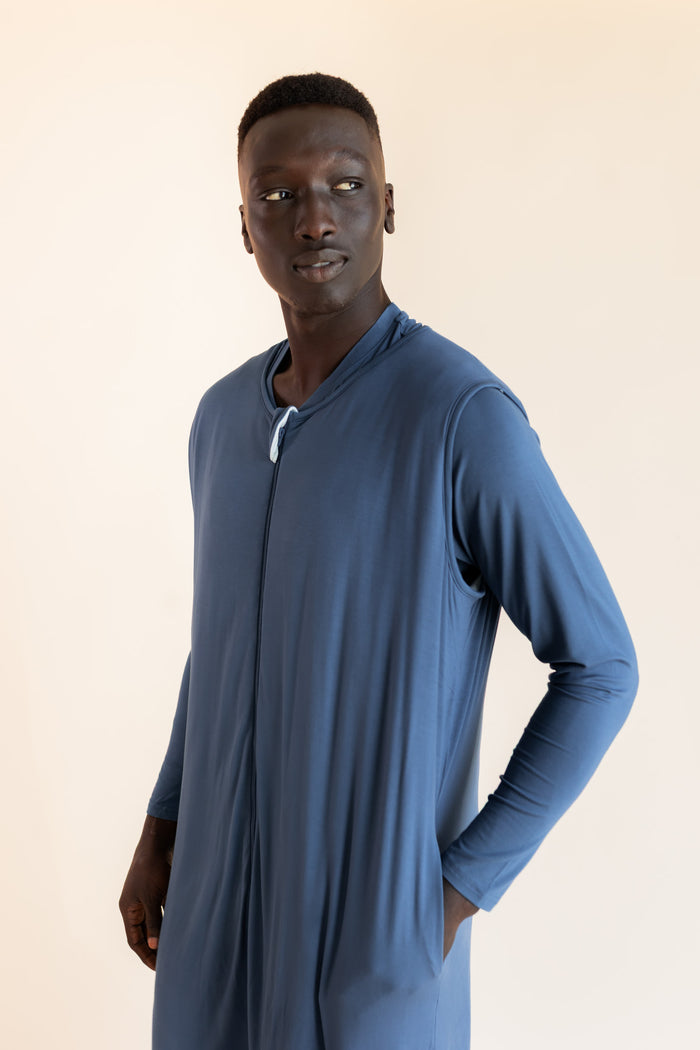 A man wearing a blue sleep sack with a front zipper, posed against a plain beige studio background.
