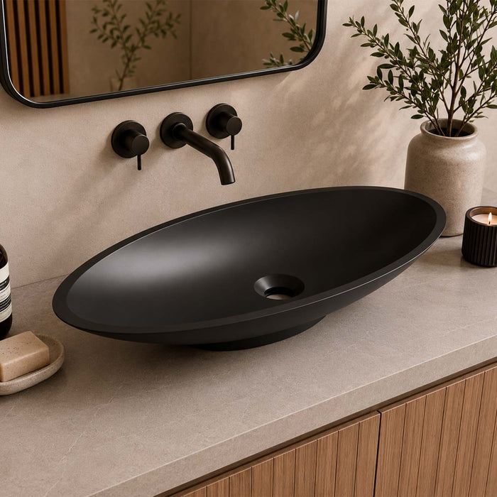 A matte black vessel sink with a matching black faucet set, shown installed on a beige stone countertop in a bathroom setting with a mirror, plants, and a candle.