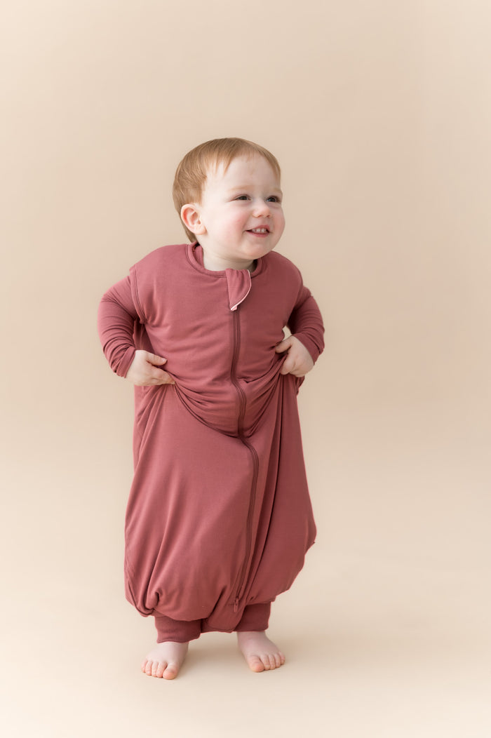 Child posing in Sleep Bag Walker in Ember 1.0 on a beige background
