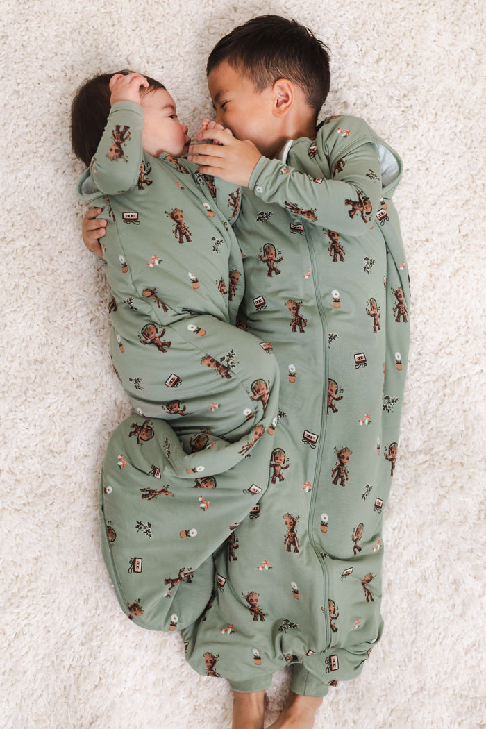 A Boy and a baby lying on a beige carpet cuddled together wearing Green Sleep Bag Walker in Groot 1.0 print and Sleep bag in Groot print