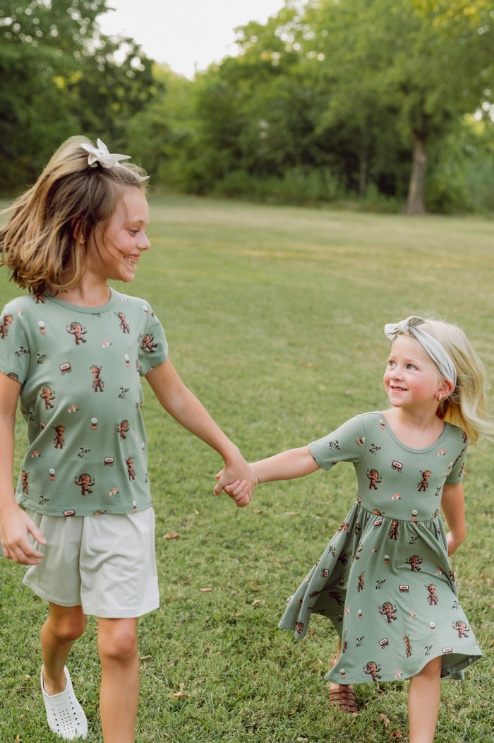 Two girls walking in grass wearing Twirl Dress and toddler basic tee in Groot print