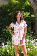 woman wearing pink short sleeve pajama set with mahjong tile print standing outdoors in greenery