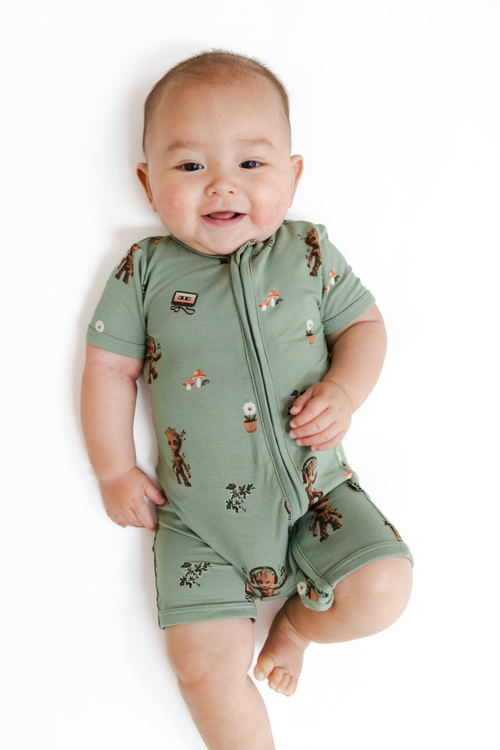 Baby in Green Zipper Shortall Romper in Groot print lying on a white background